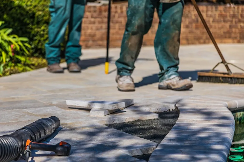 Construction workers installing stone patio pavers during outdoor landscaping project